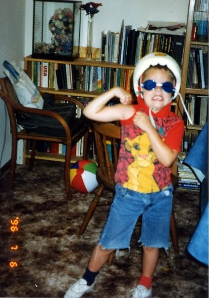 Aslan as a child, posing in a helmet, blue sunglasses and a Lion King shirt.